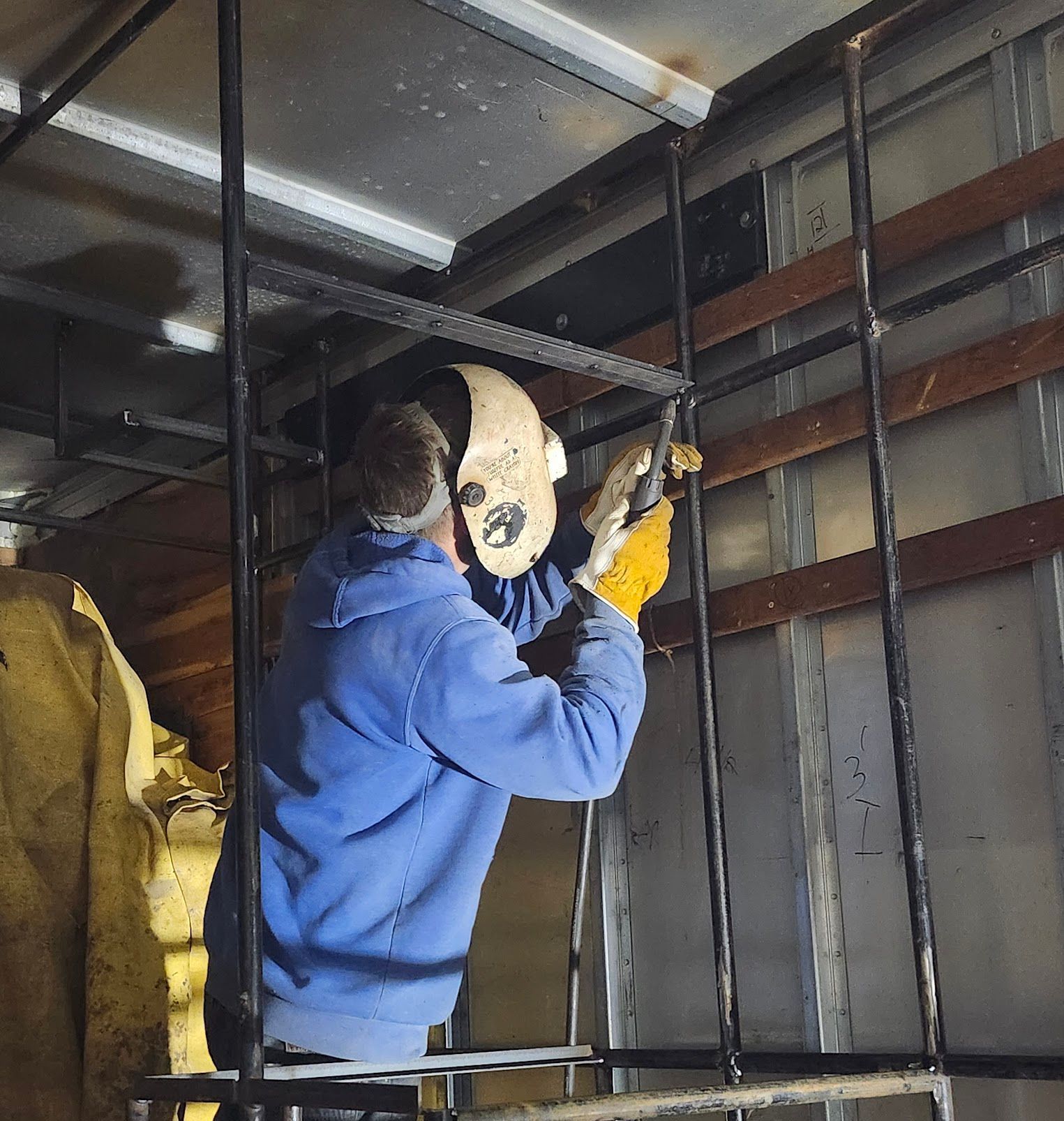 A man wearing a welding helmet is working on a metal structure