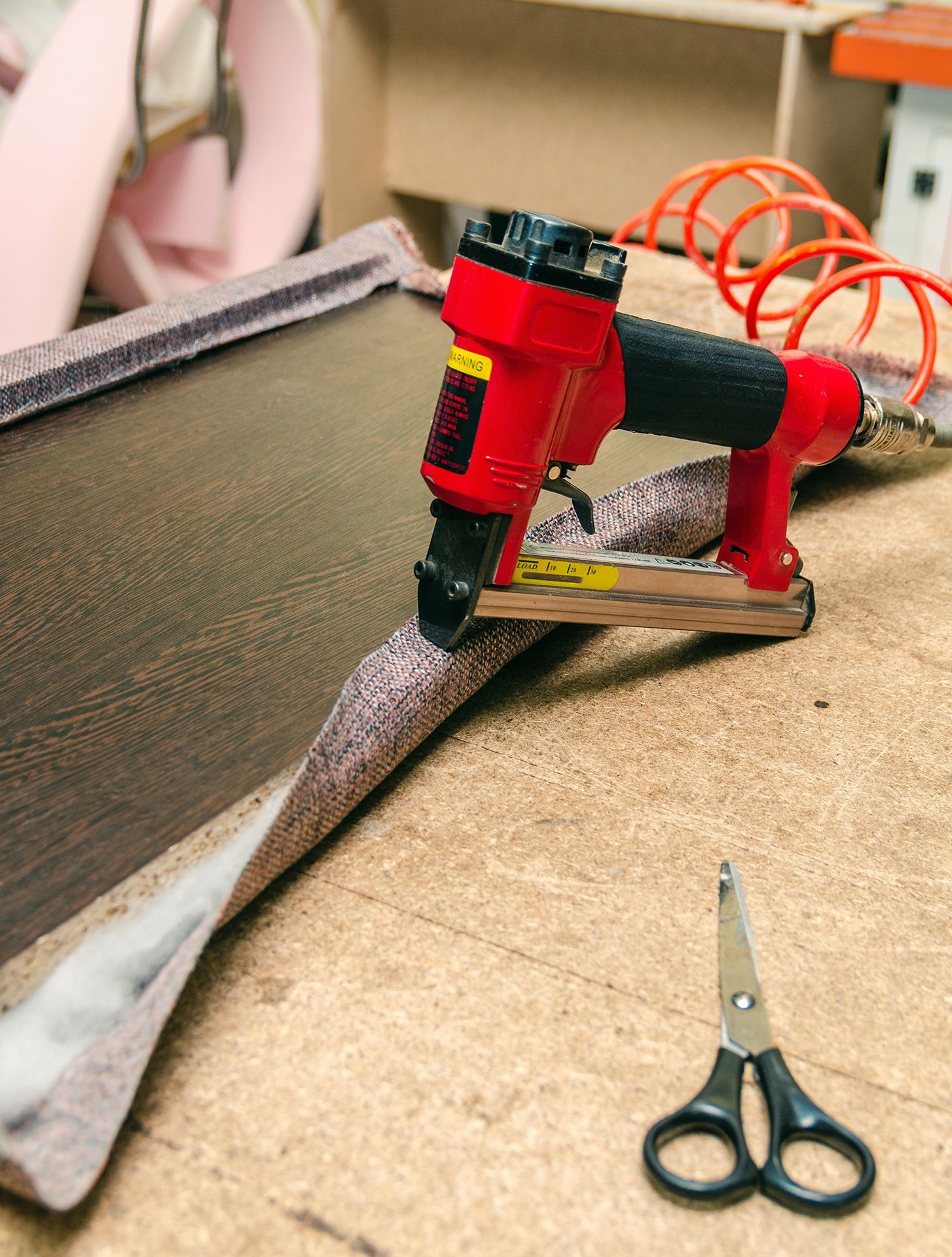 Una grapadora roja está sobre una mesa de madera al lado de un par de tijeras.