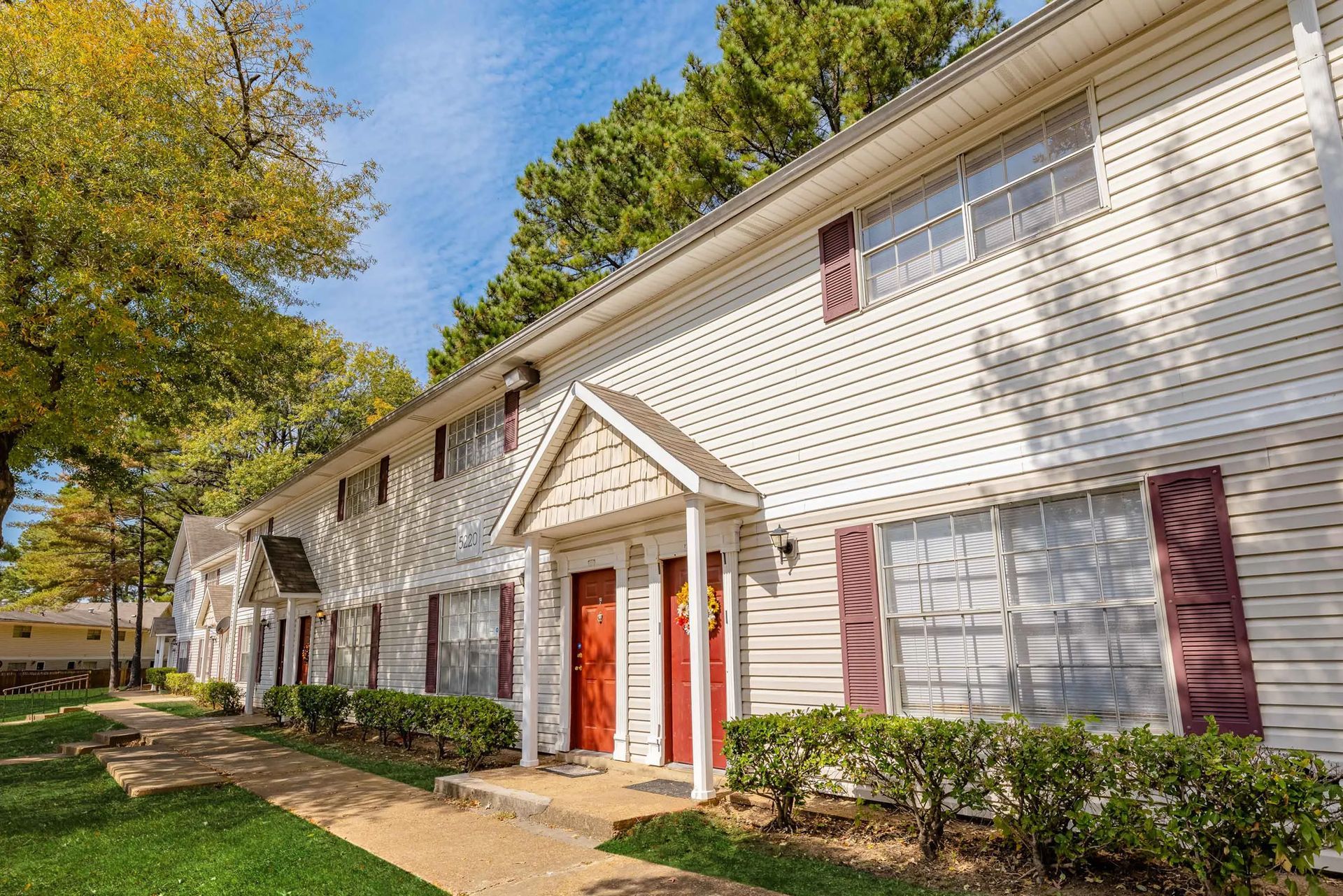 A white apartment building with red shutters and a porch.
