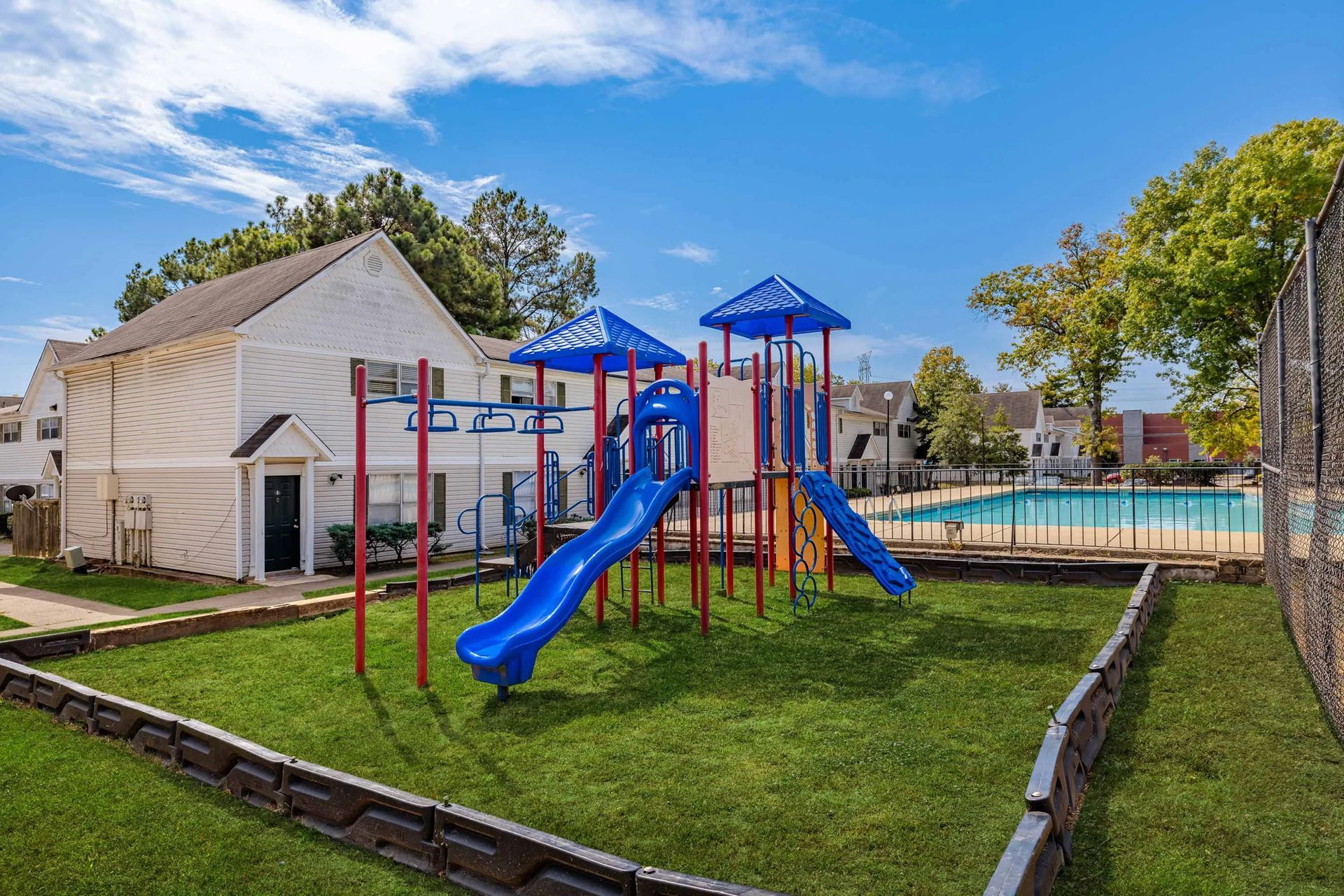A playground with a slide , swings , and a swimming pool in front of a house.