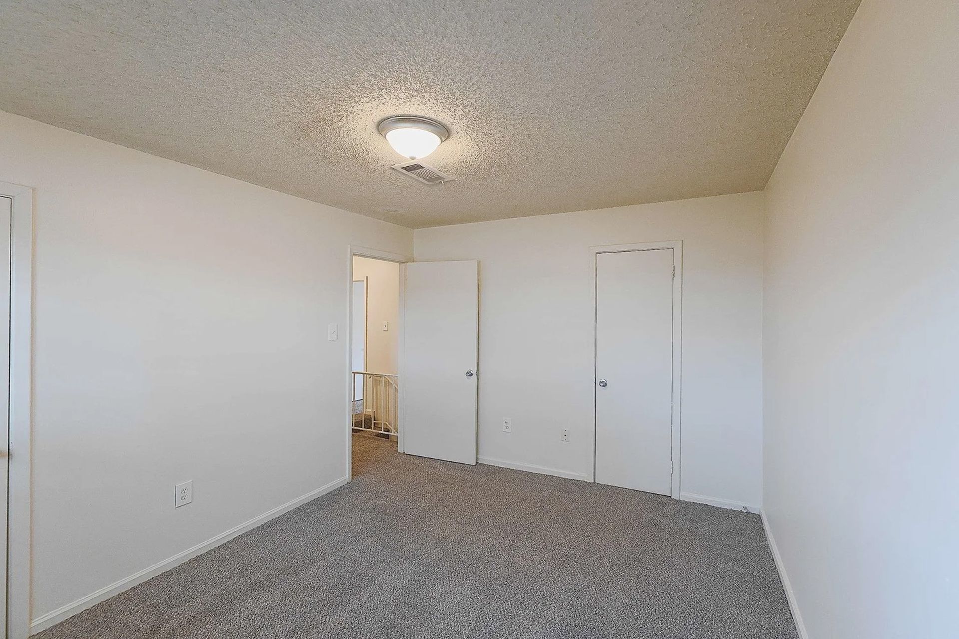An empty bedroom with a carpeted floor and white walls.