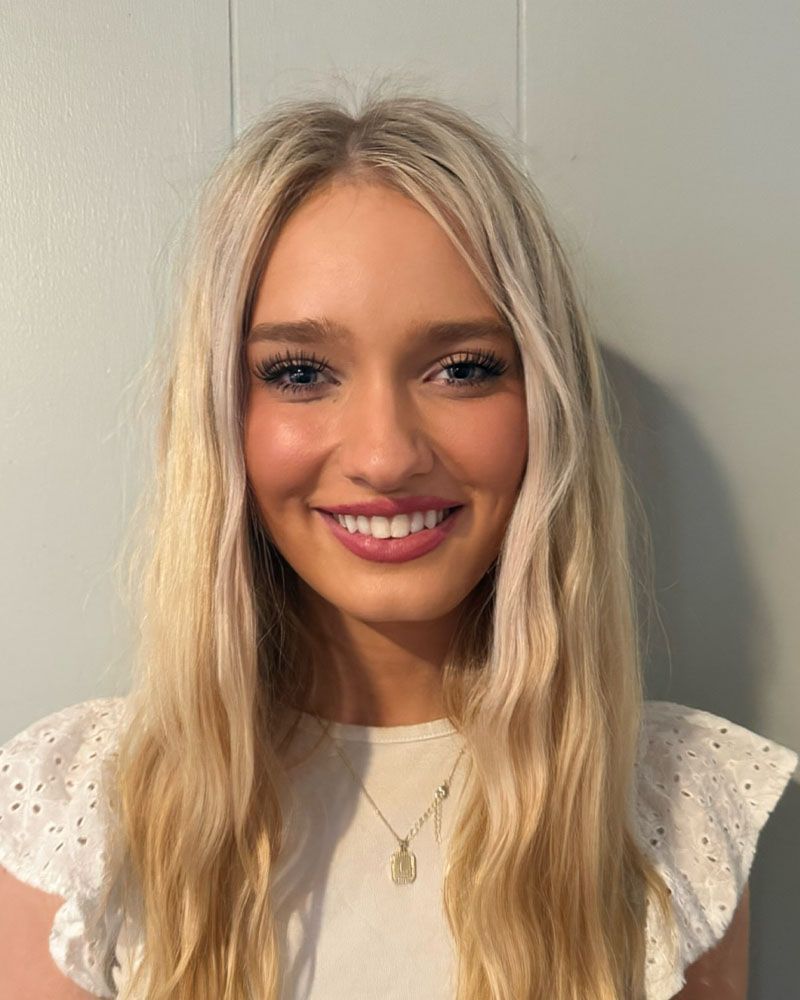 A blonde woman wearing a black dress and earrings is smiling for the camera.