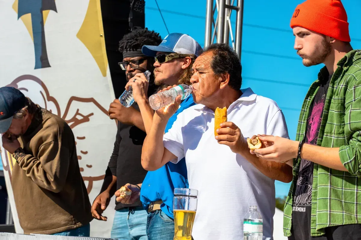 A group of people are standing next to each other eating food and drinking water.