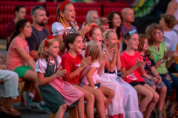 Children and adults clapping and cheering at an outdoor performance.