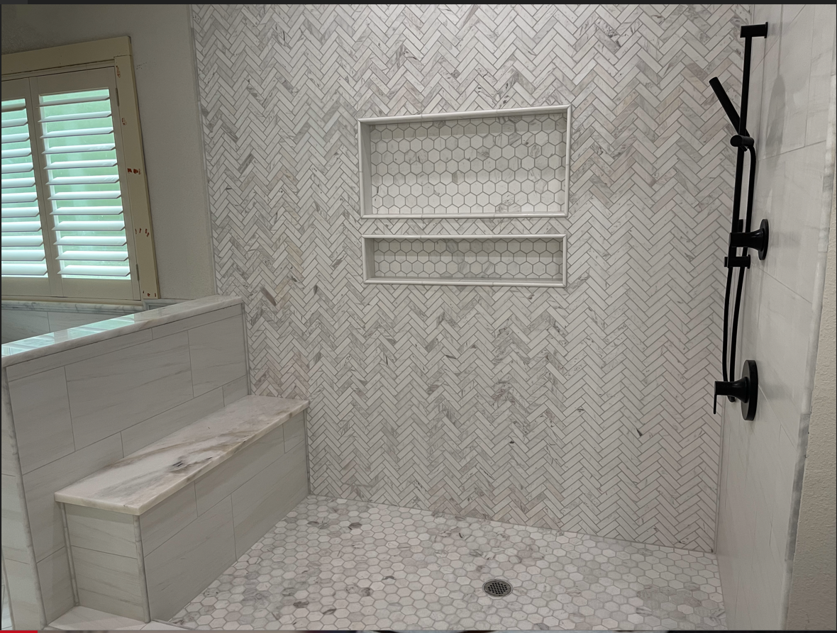 A bathroom with a walk in white tile shower and a bench