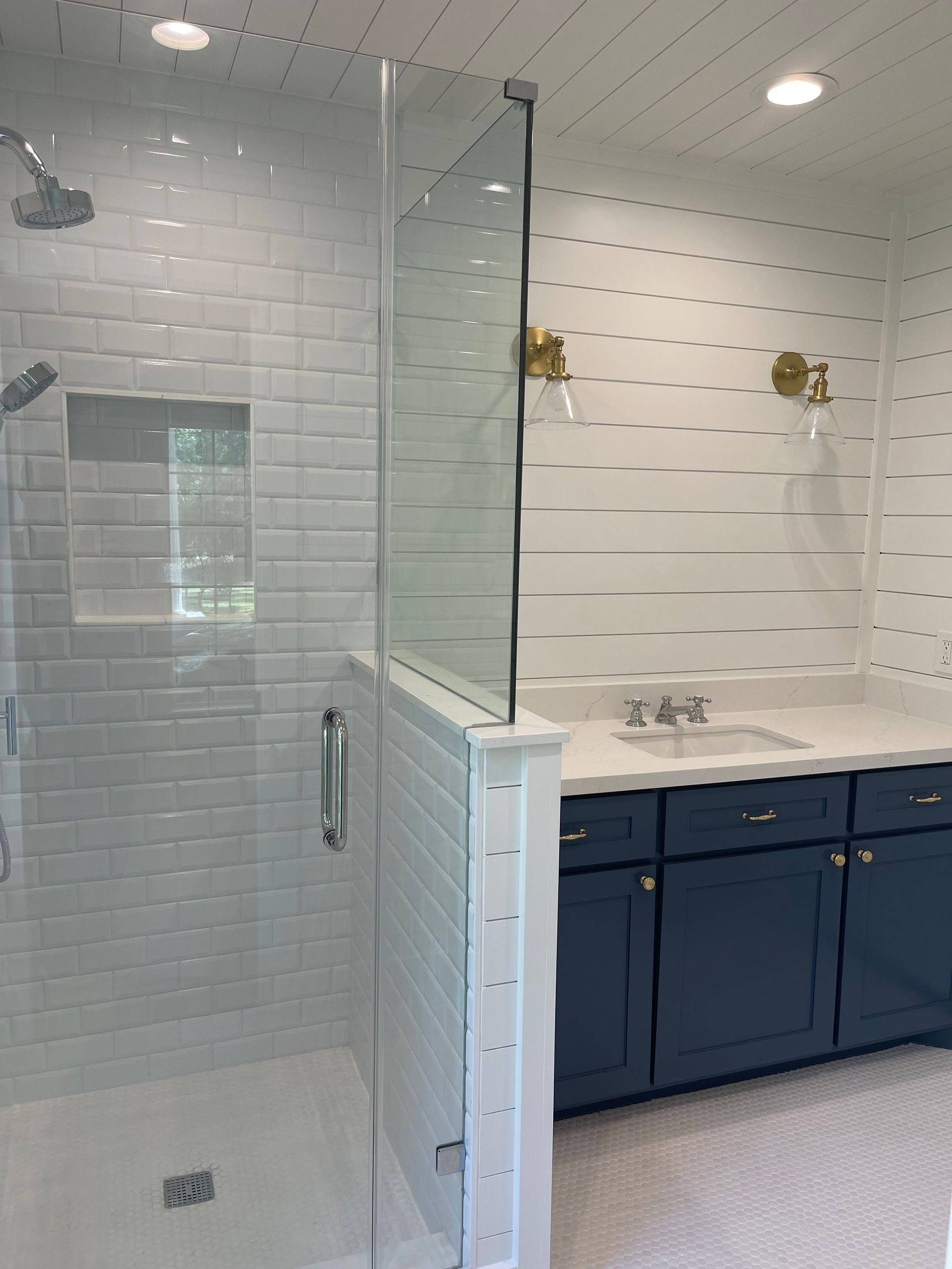 A bathroom with a subway tile walk in shower and a blue vanity with a sink