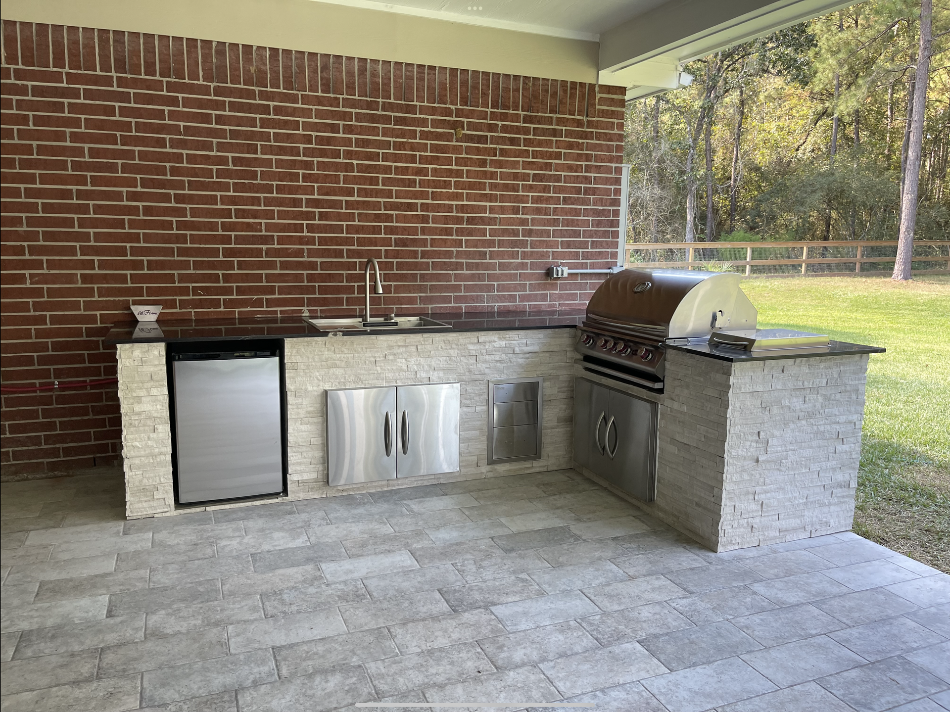 An outdoor kitchen with a brick wall and a grill