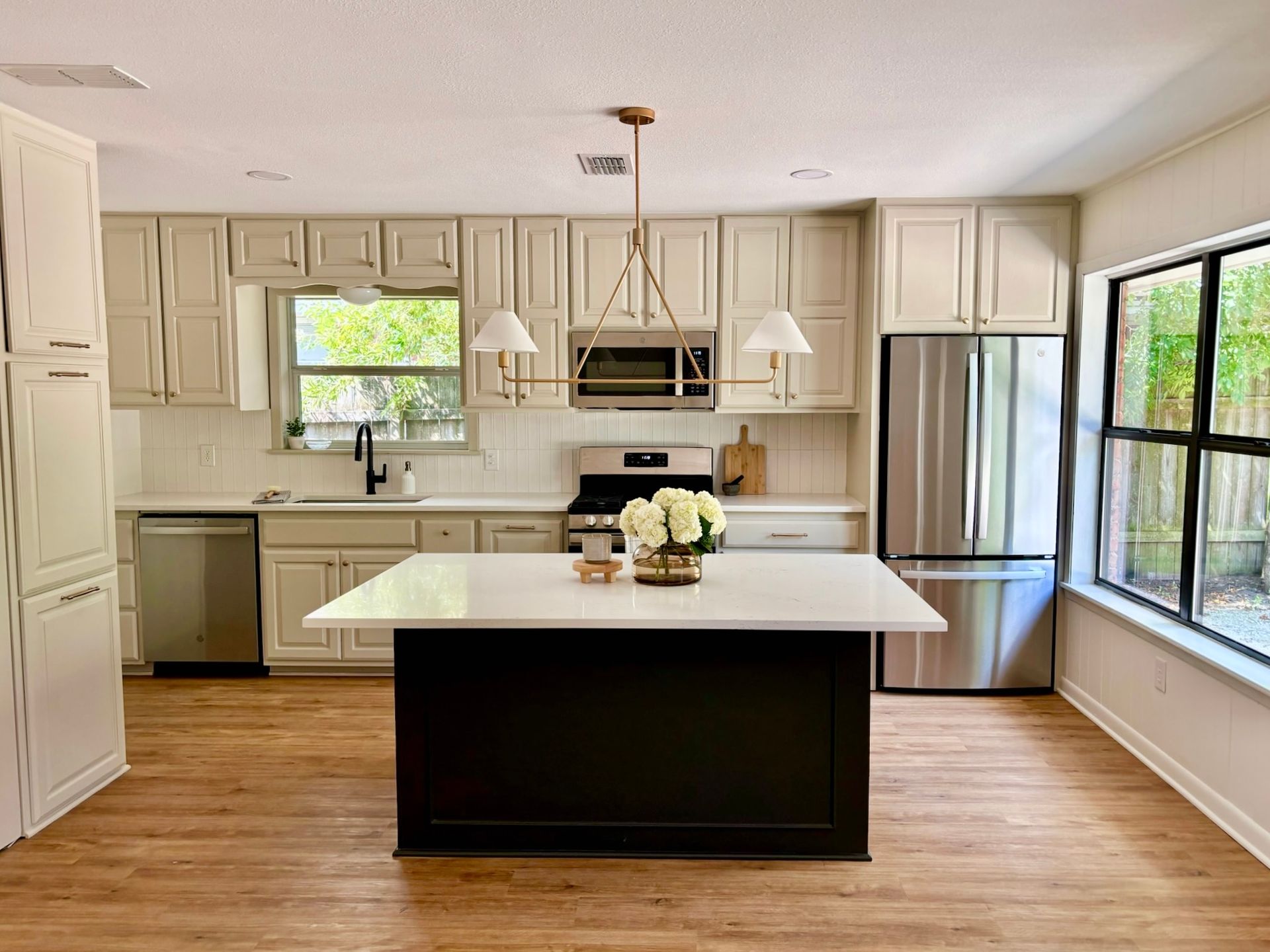 A kitchen with white cabinets , stainless steel appliances , a large island and a window.