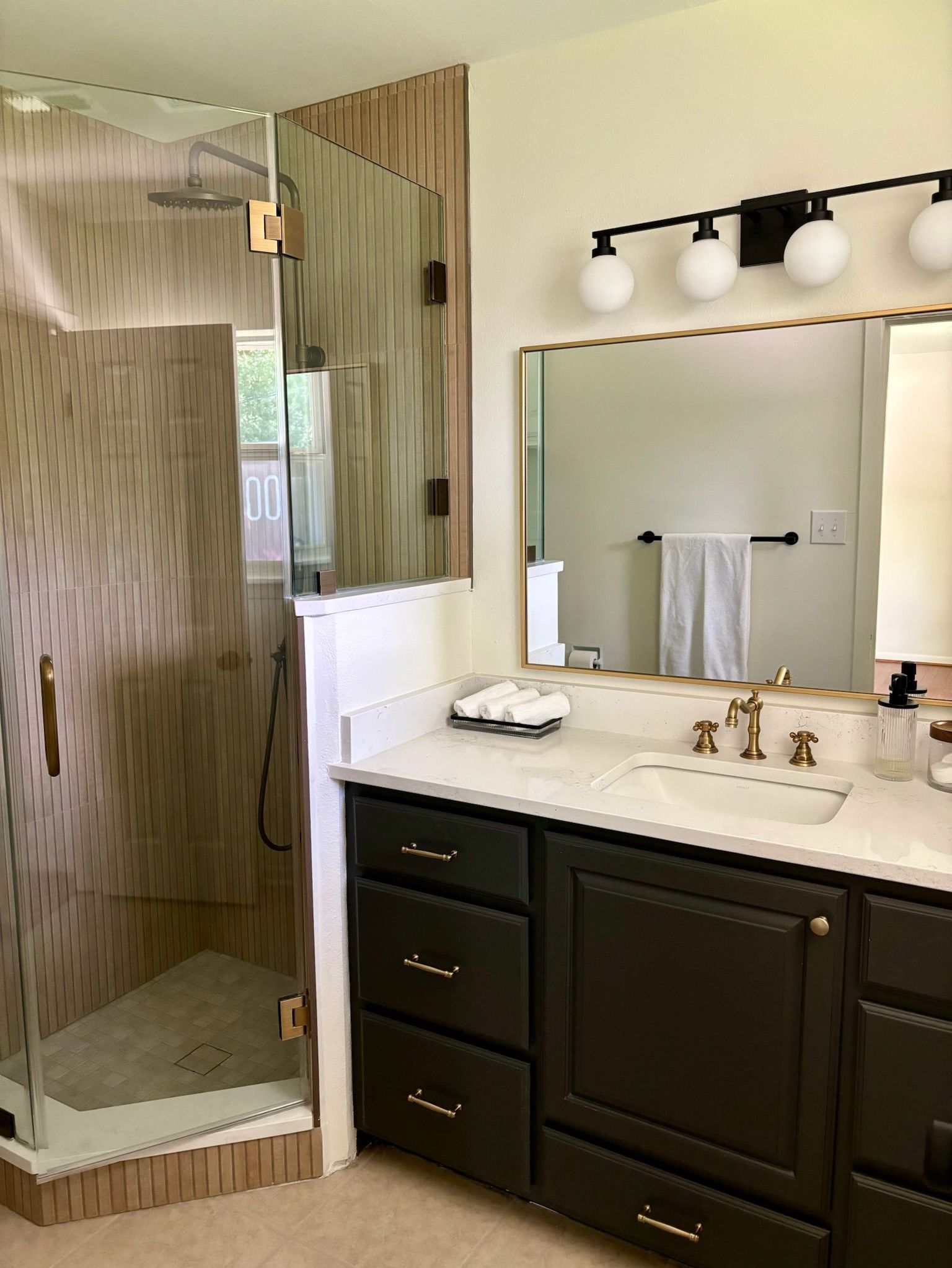 A bathroom with a walk in shower , sink , mirror and vanity.