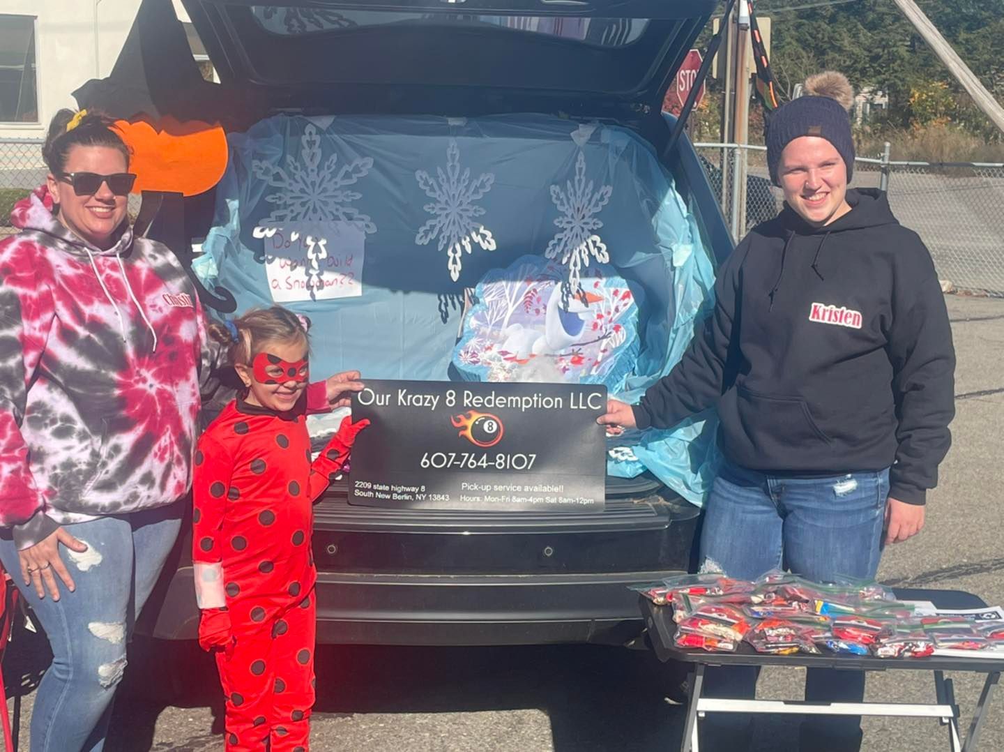 Two women and a child are standing in front of a trunk filled with candy.