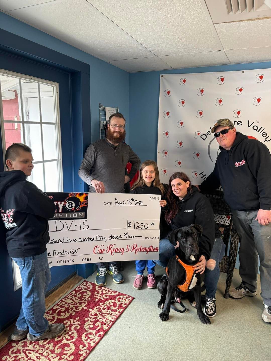 A group of people standing around a dog holding a check.