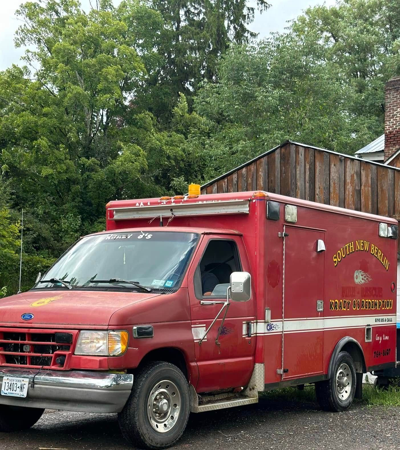 A red ambulance is parked in front of a wooden building