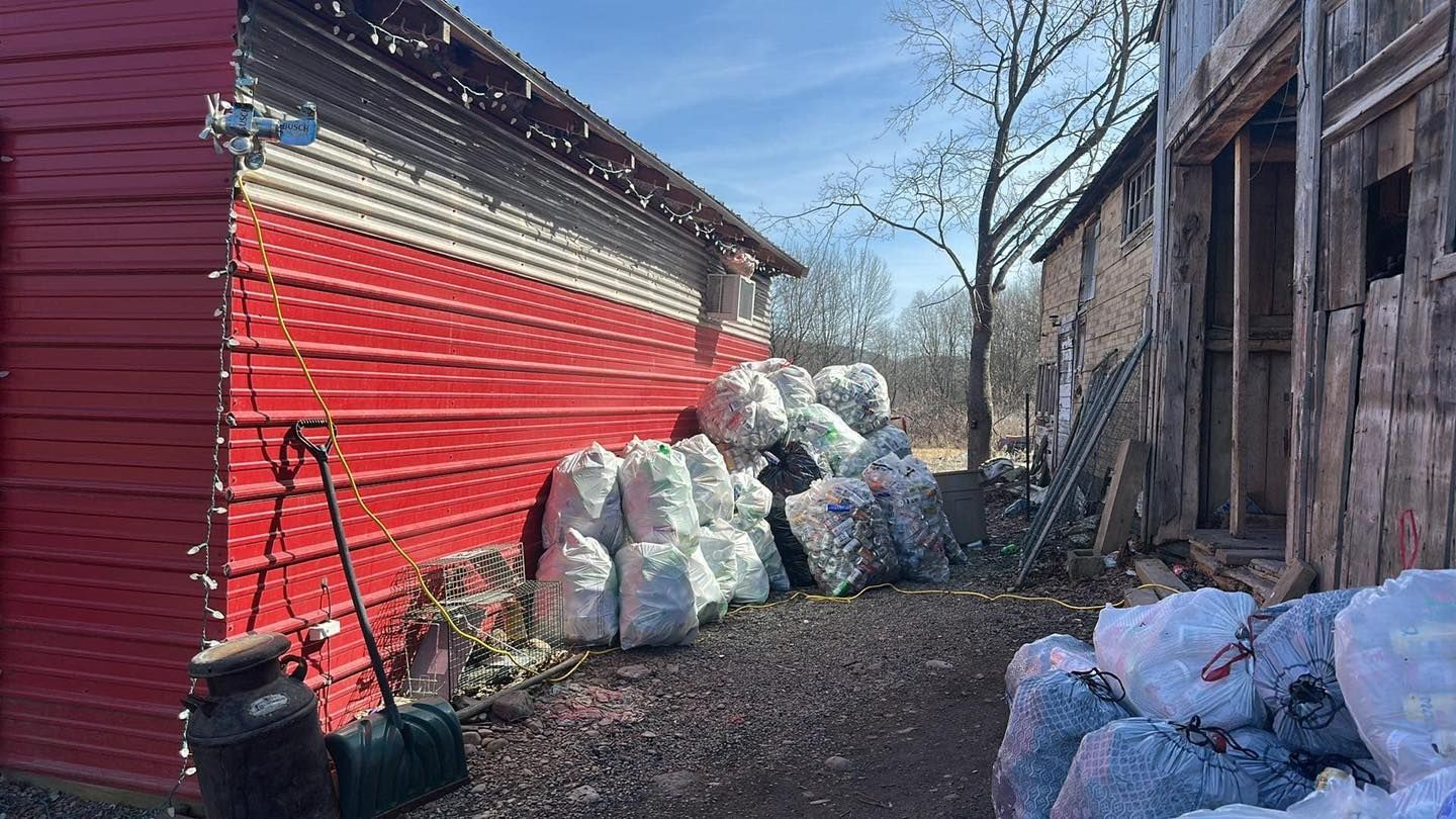 A pile of christmas trees is sitting in front of a red barn.
