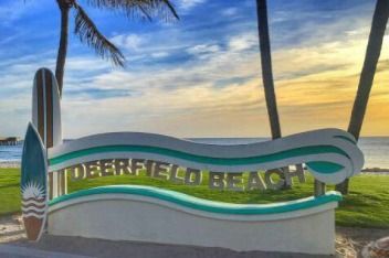 A sign that says deerfield beach with palm trees in the background