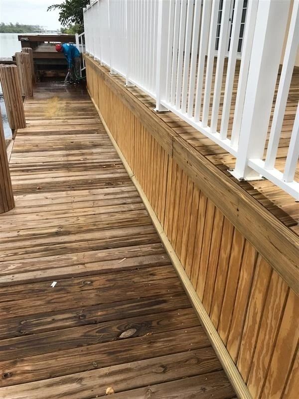 A man is standing on a wooden dock next to a white railing.