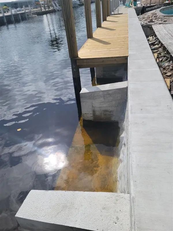 A wooden dock is sitting next to a concrete wall in the water.