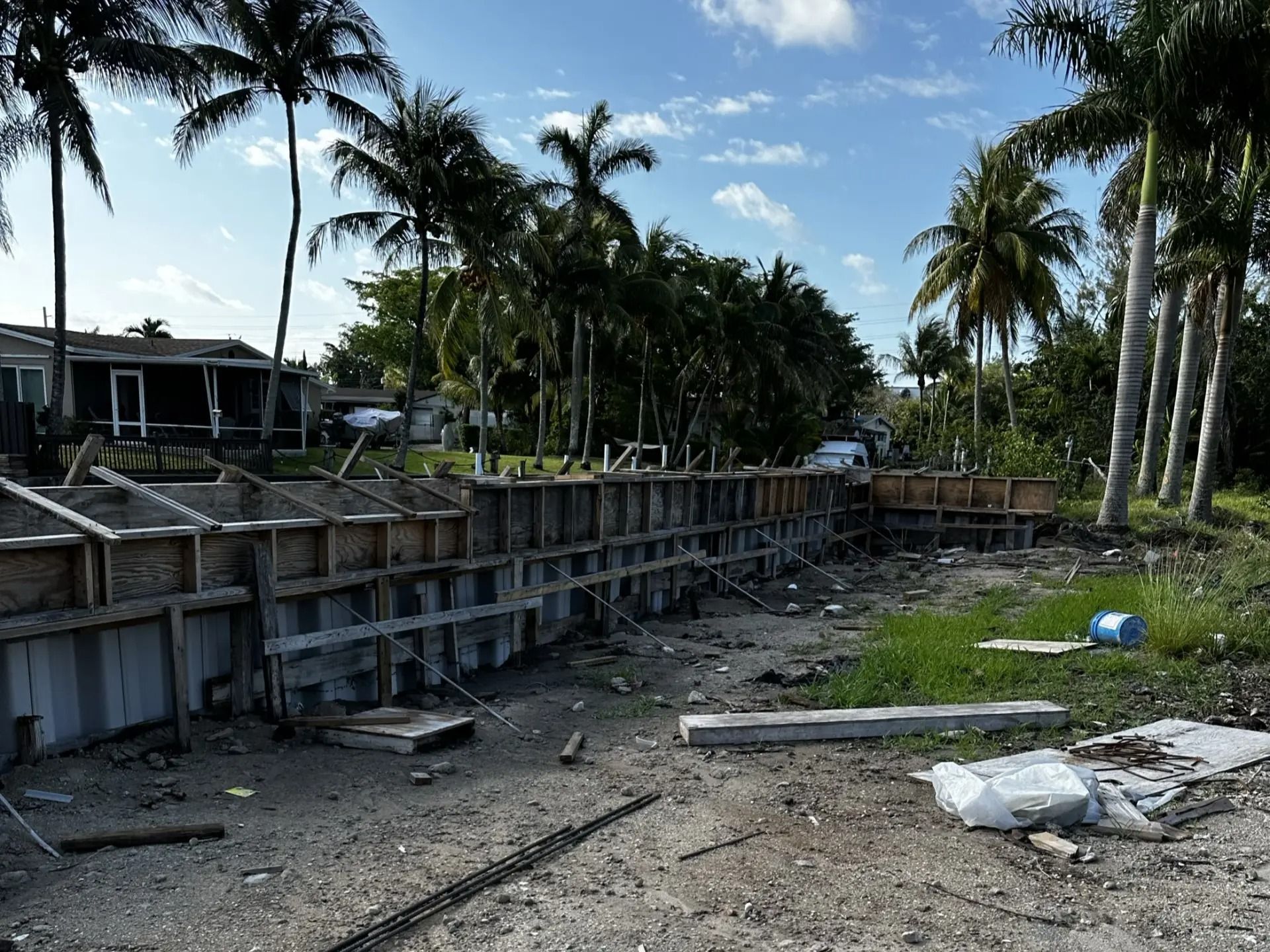 A construction site with palm trees in the background and a house in the background.
