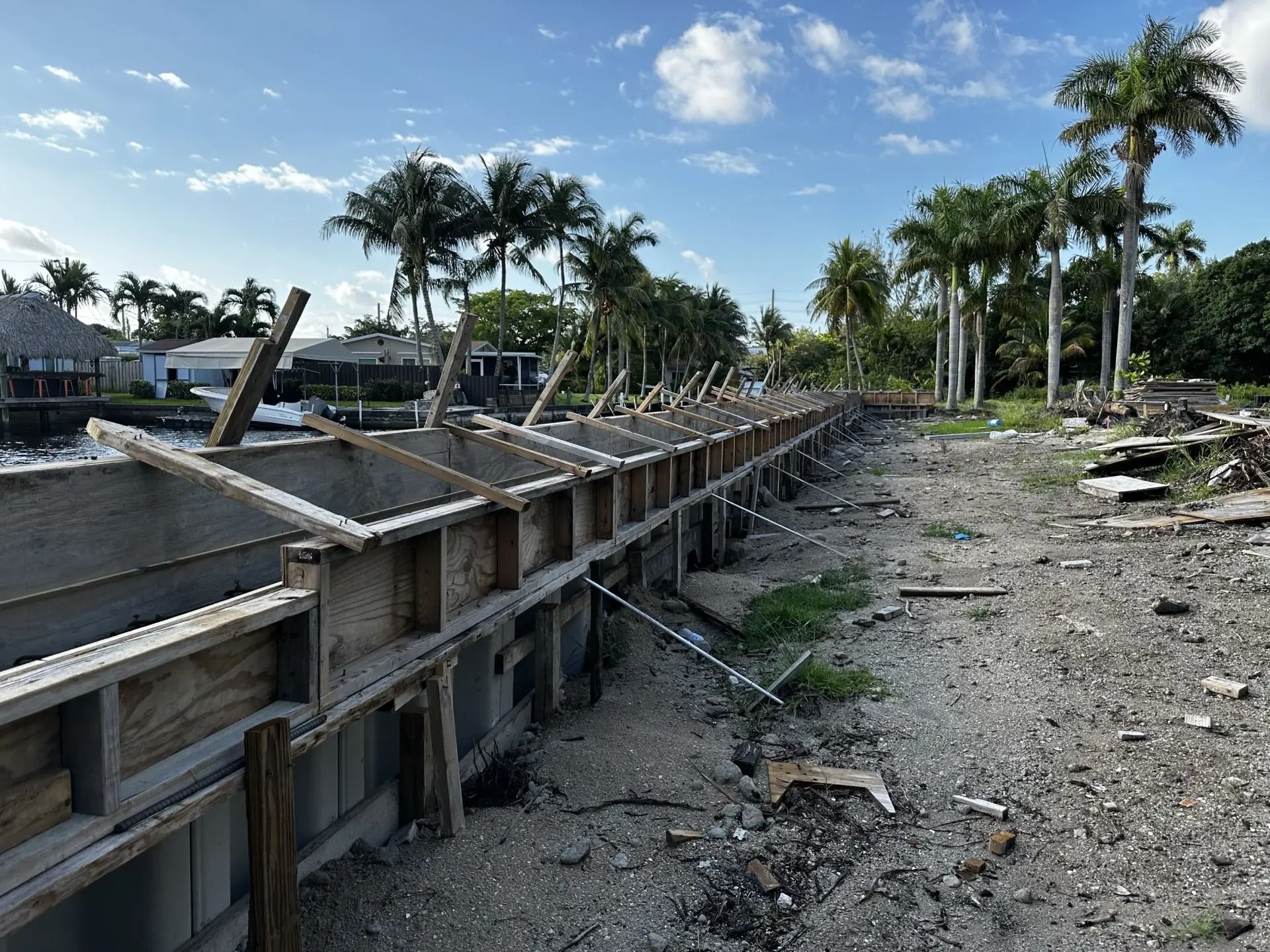 A concrete wall is being built in the middle of a dirt field with palm trees in the background.