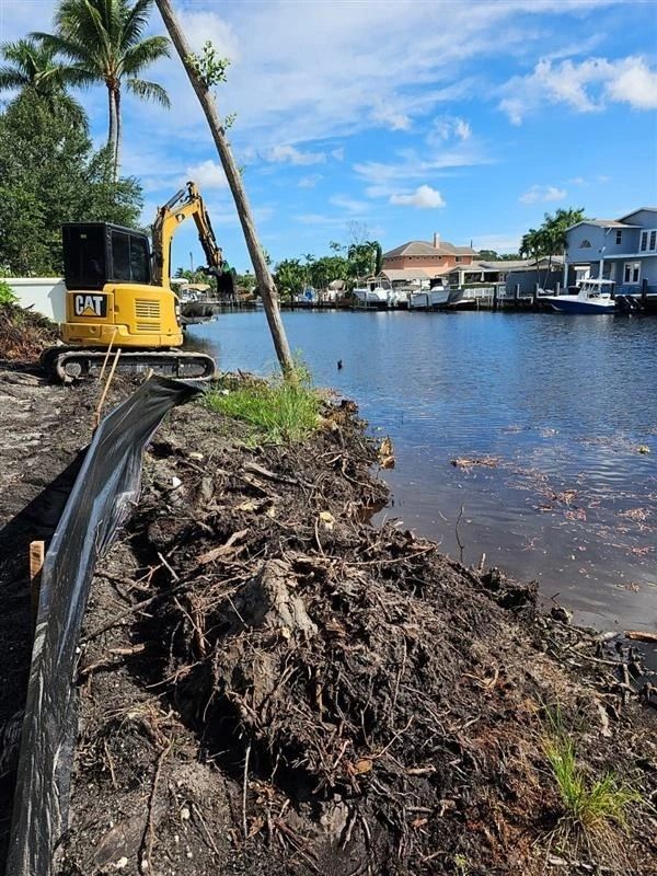 A yellow cat excavator is working on the shore of a body of water