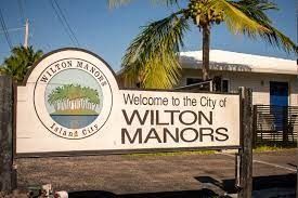 A welcome to the city of wilton manors sign with palm trees in the background.