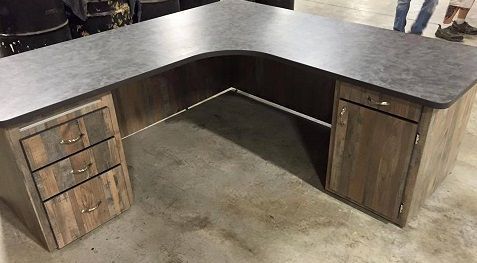 A wooden desk with drawers and a black top is sitting on a concrete floor.
