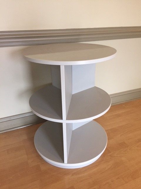 A round table with three shelves on a wooden floor
