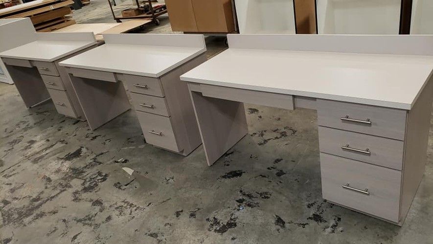 A row of white desks with drawers in a warehouse.