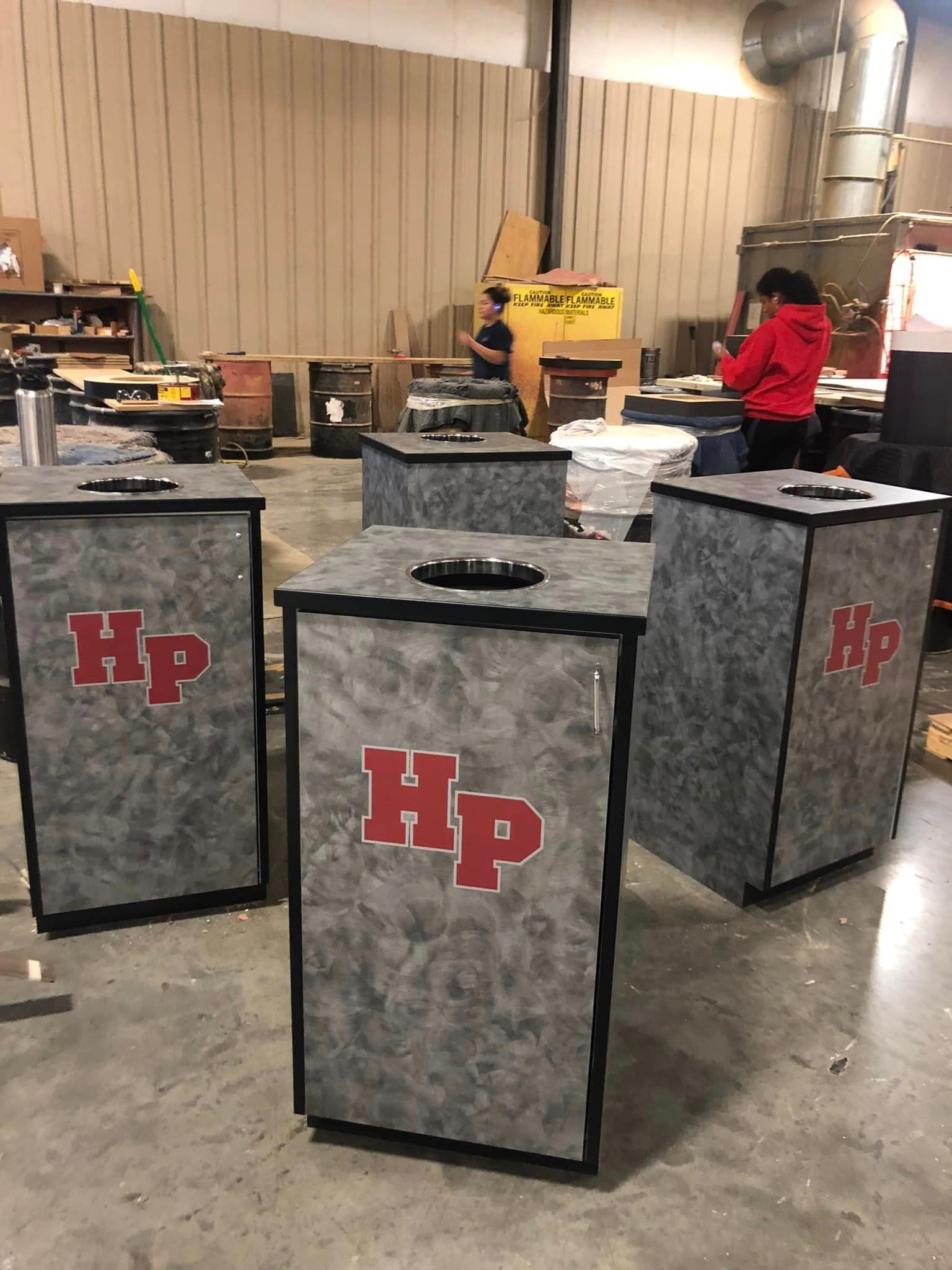 Three trash cans with hp written on them are sitting in a warehouse.