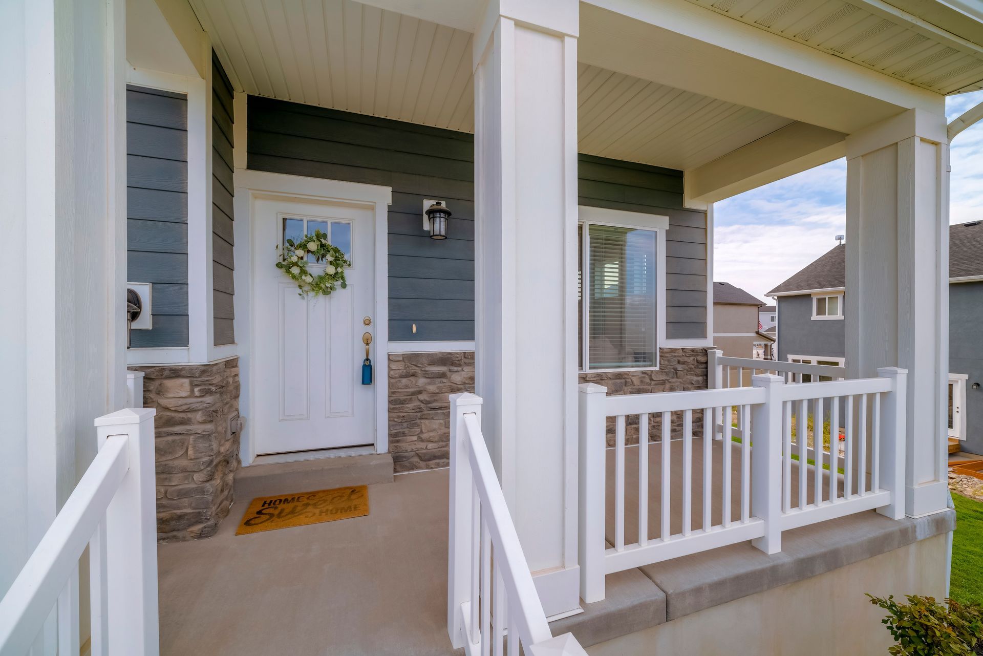 The front porch of a house with a white railing and a wreath on the door.