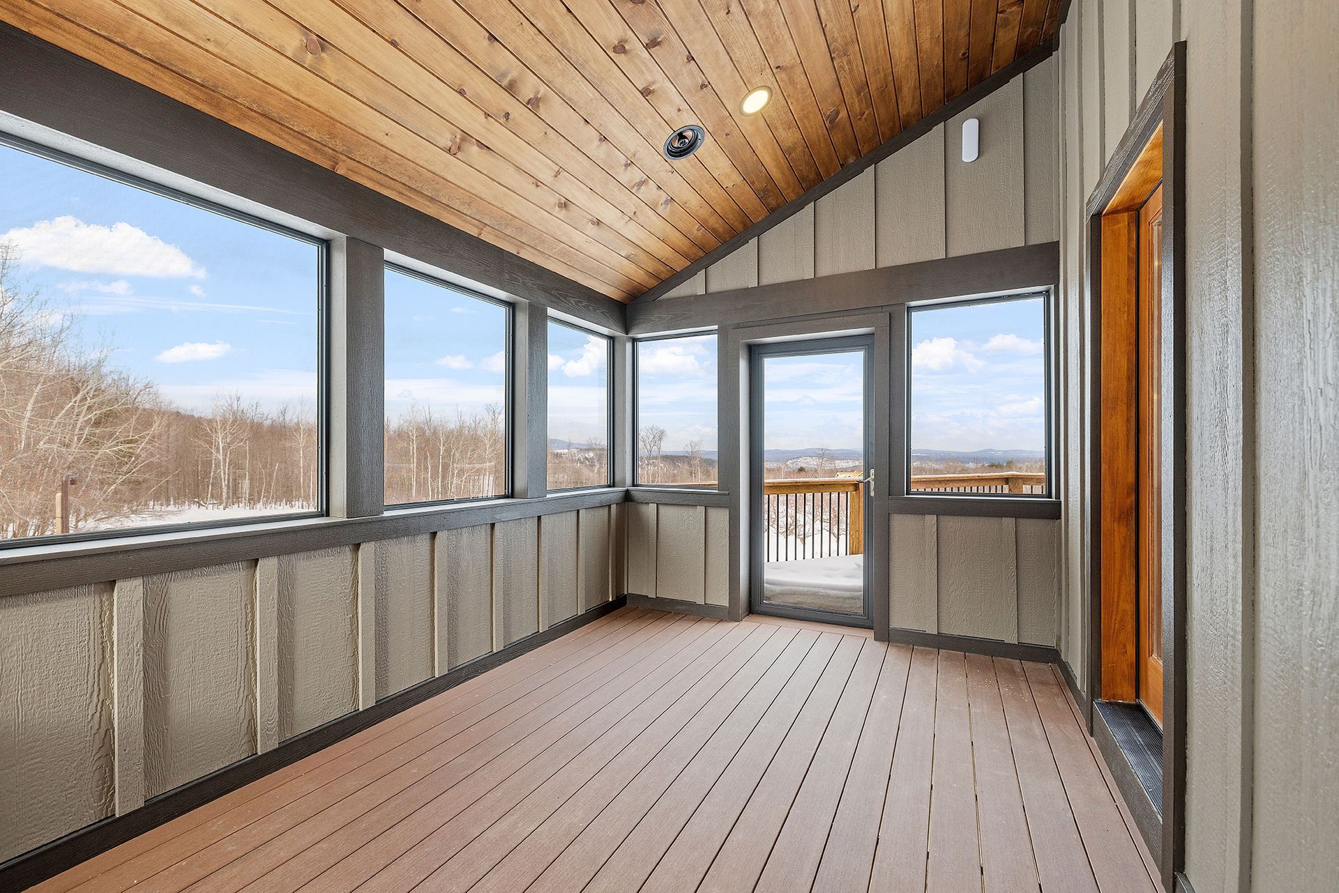 A screened in porch with a wooden ceiling and lots of windows.