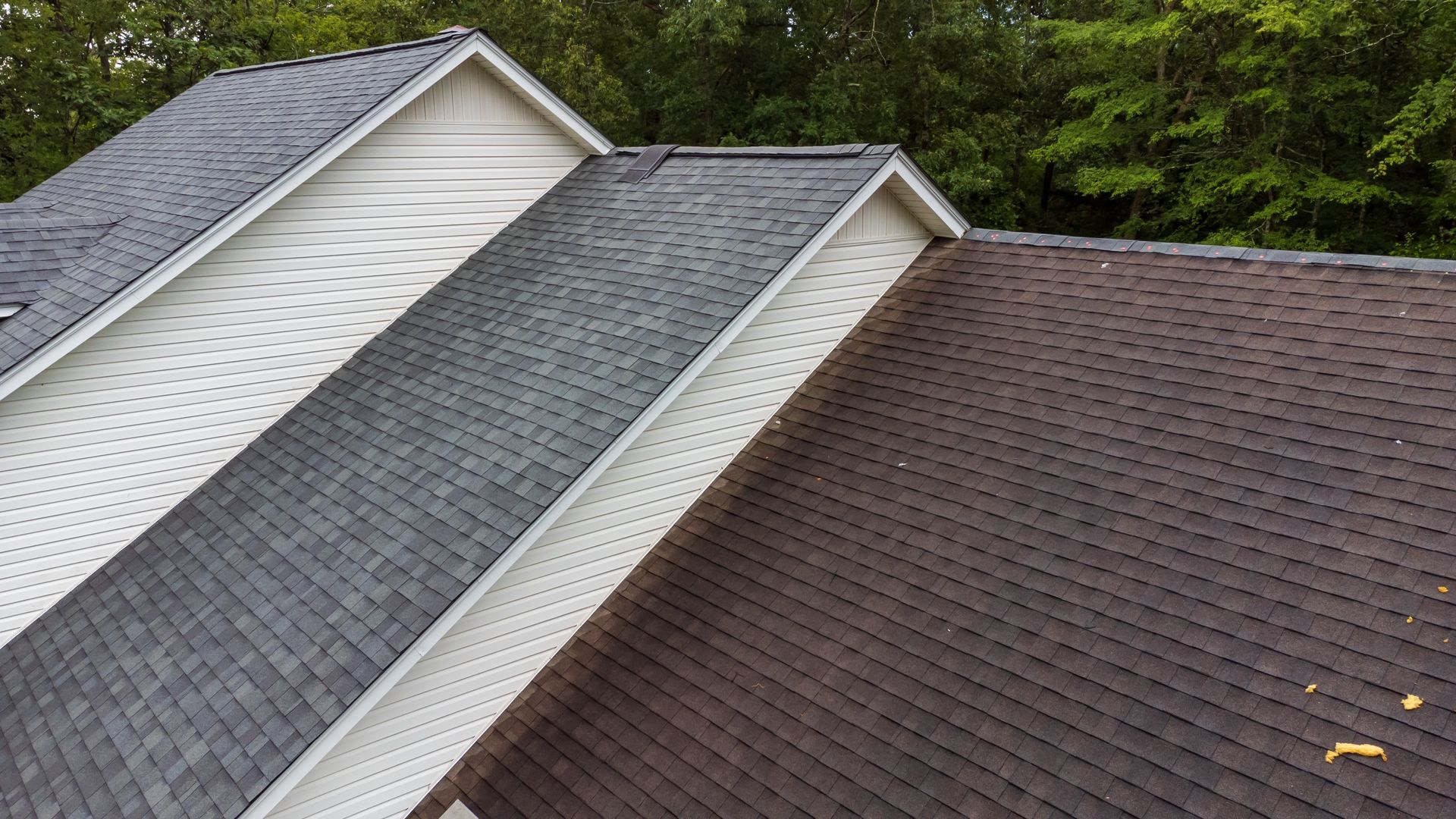 The roof of a house has three different colored shingles on it.