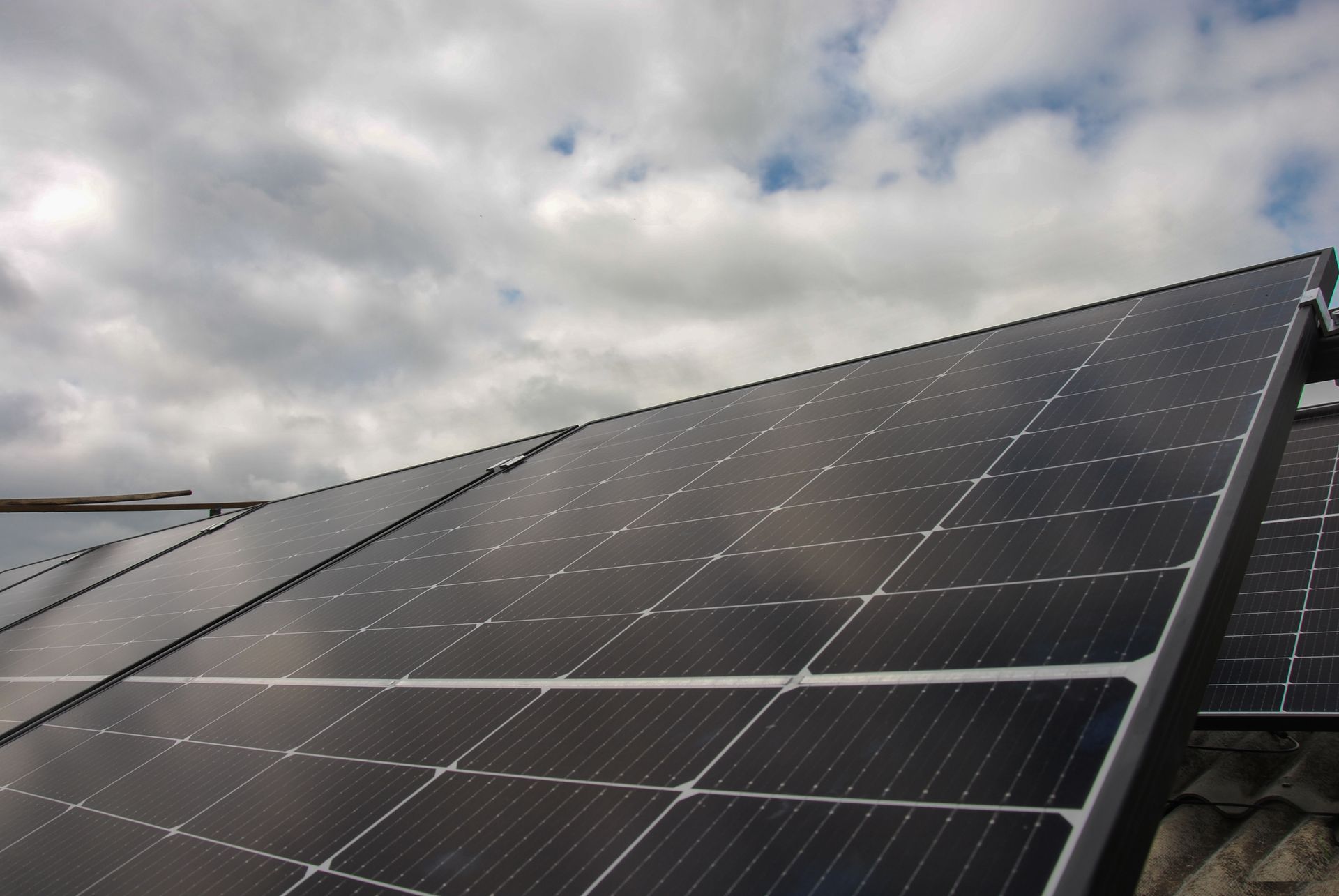 A row of solar panels on a roof with a cloudy sky in the background
