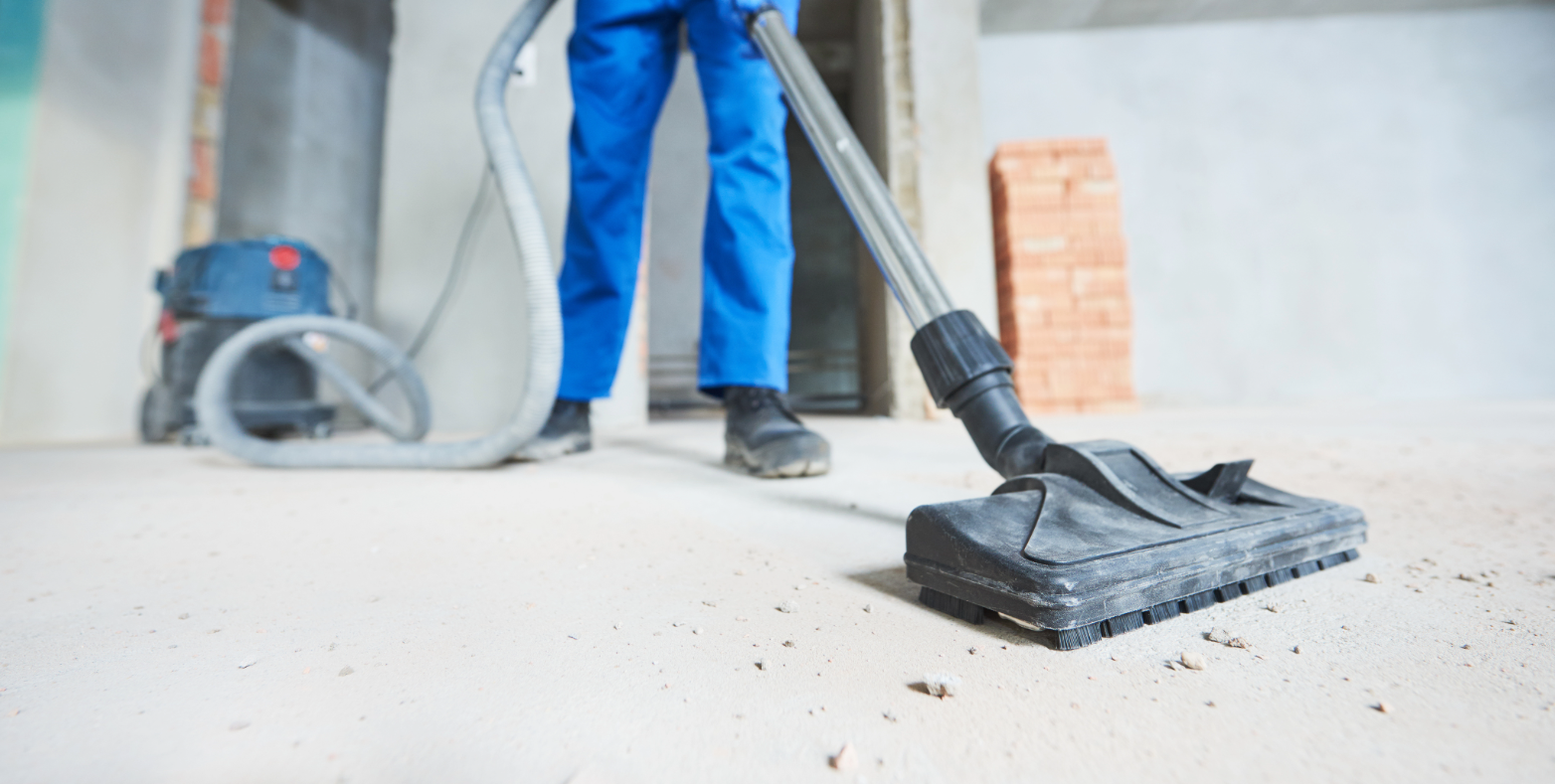 A person wearing blue hoovering dust on a construction site.