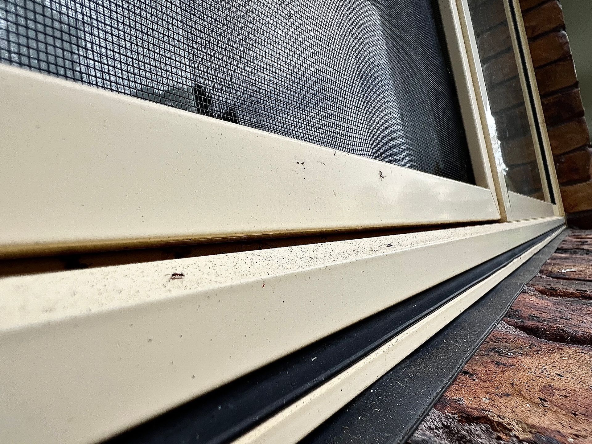 Close-up of a cream-colored window frame with a screen, set against a brick exterior.