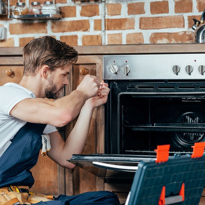 Young technician in protective workwear, performing appliance repair in a residential kitchen. Young technician in protective workwear, performing appliance repair in a residential kitchen.