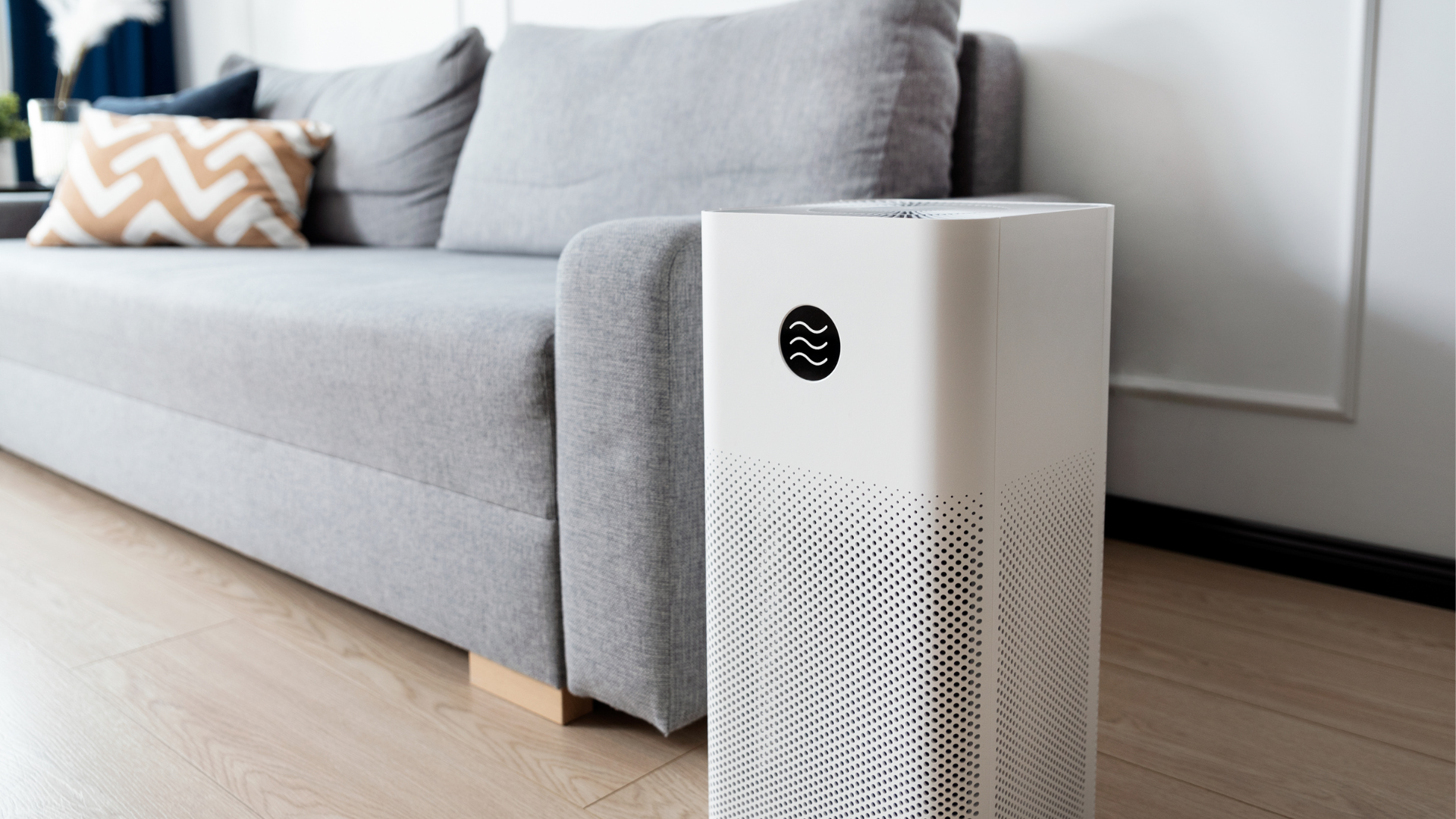 A white air purifier is sitting next to a couch in a living room.