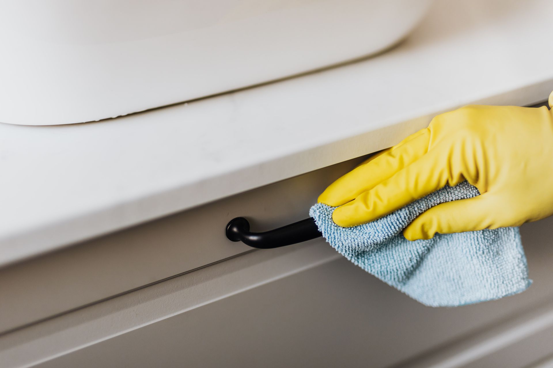 A person wearing yellow gloves is cleaning a cabinet with a towel.
