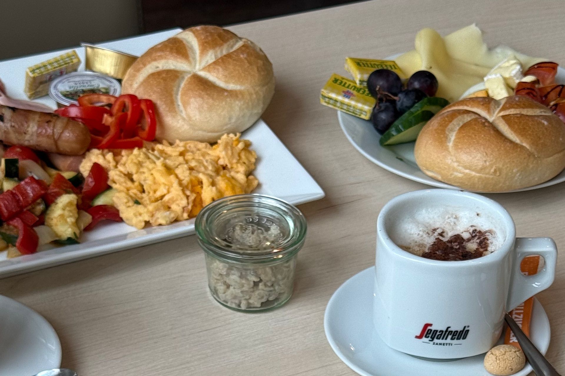 Ein reichhaltiges Frühstück mit Obst, Süßspeisen, Schinken, Gemüse, Avocado, Croissant und Salaten sowie einem Orangensaft