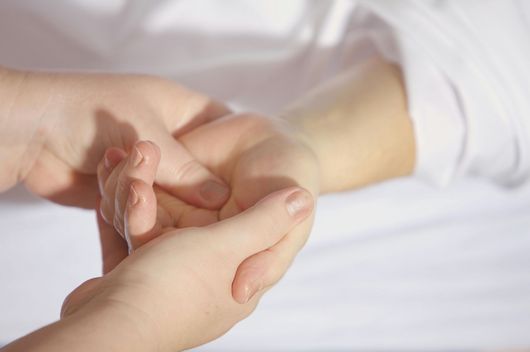 Hands gently holding a small hand on a white bed