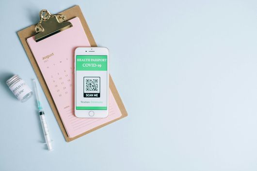 A cell phone is sitting on top of a clipboard next to a syringe and a bottle of vaccine.