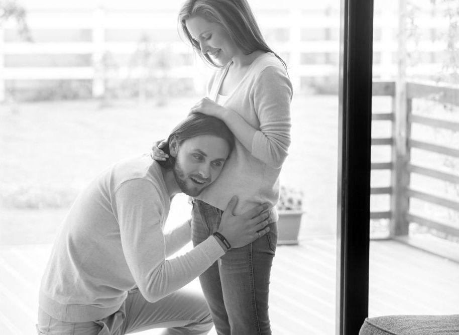 A man is hugging a pregnant woman 's belly in a black and white photo.