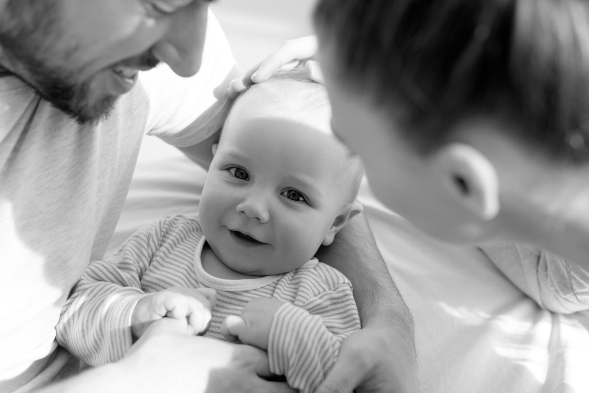 A happy couple looking at a smiling baby.