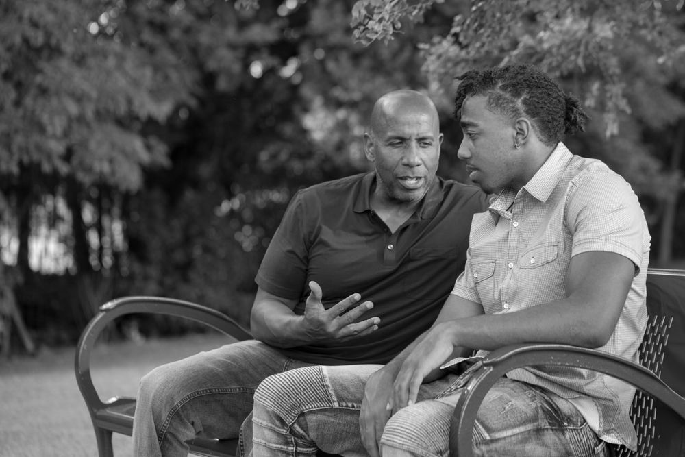 Two men are sitting on a park bench talking to each other.