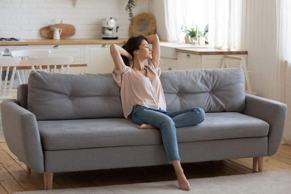 A woman is sitting on a couch in a living room stretching her arms.