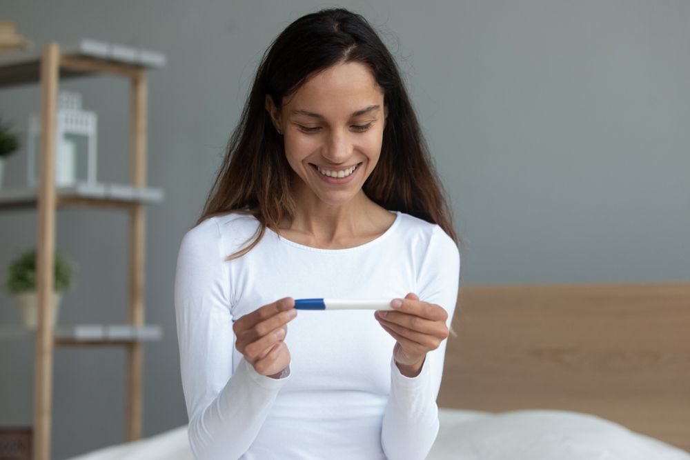 A woman is sitting on a bed holding a pregnancy test.