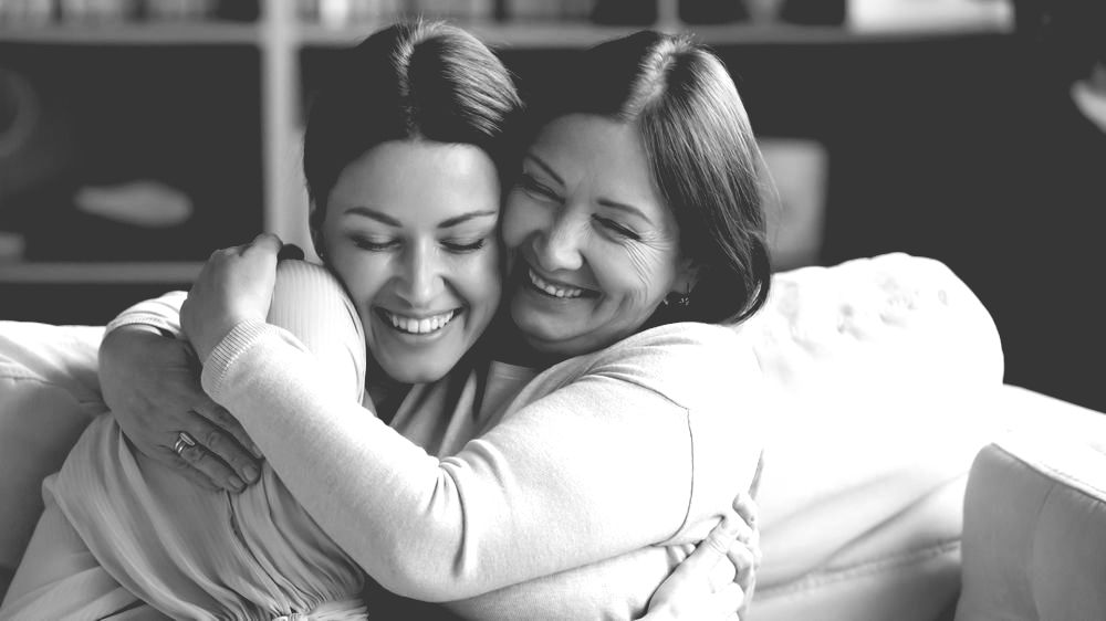 Two women are hugging each other on a couch.