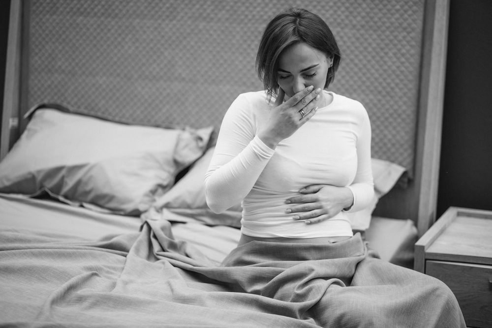 A pregnant woman is sitting on a bed with her hand on her stomach.