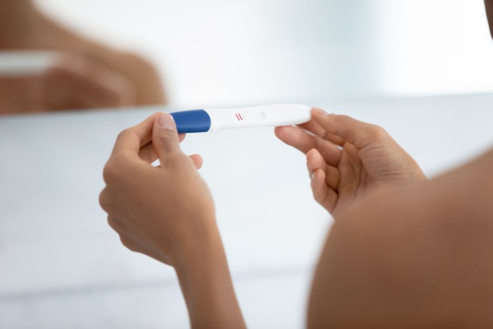 A woman is holding a pregnancy test in front of a mirror.