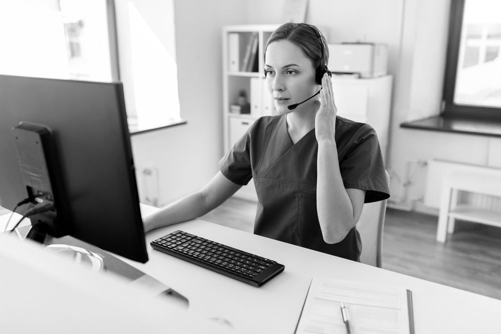 A nurse is talking on a headset while sitting in front of a computer.