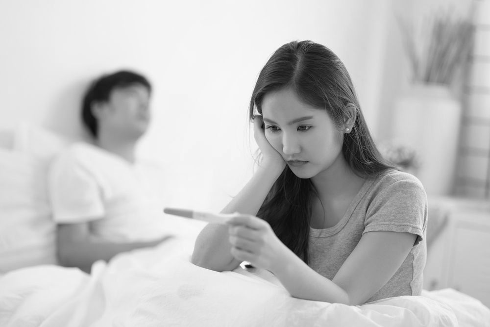 A woman is sitting on a bed holding a pregnancy test.